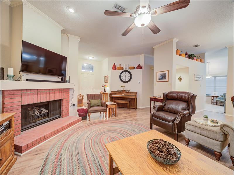 Living room featuring ceiling fan, a fireplace, a textured ceiling, light wood-type flooring, and crown molding