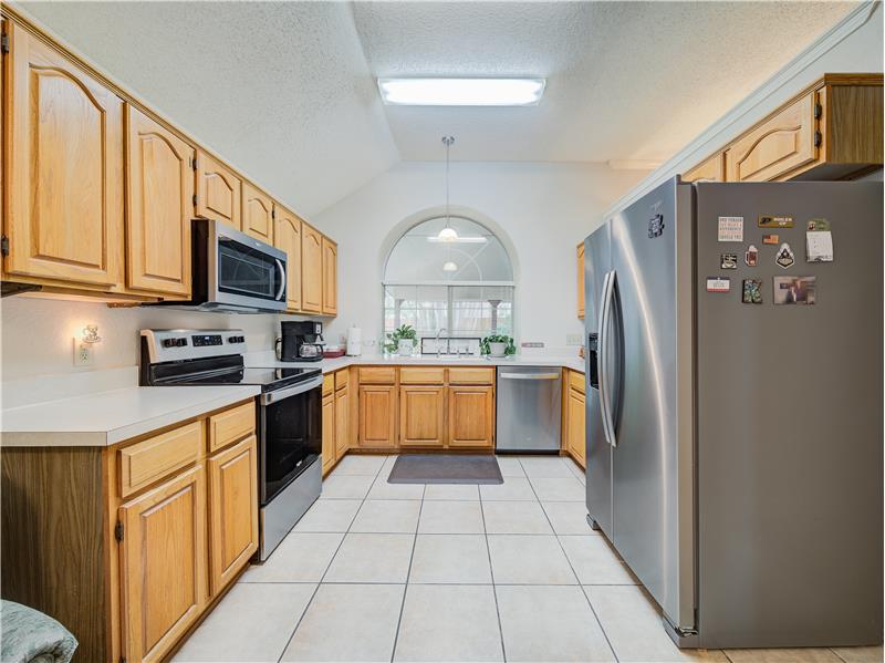 Kitchen featuring appliances with stainless steel finishes, a textured ceiling, light tile floors, and vaulted ceiling