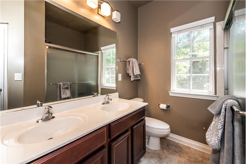 Hall bath shared by the secondary bedrooms features double-sink vanity, tile floor, extended step-in shower, linen closet.