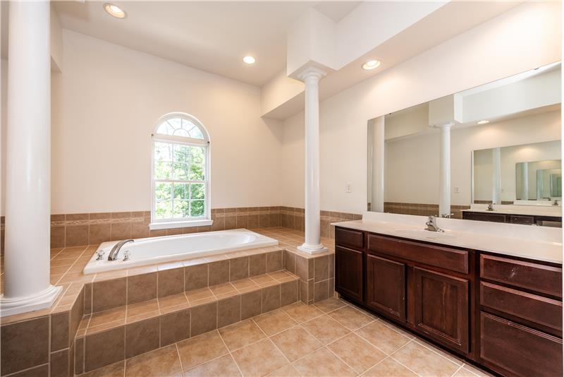 Spa-inspired owner's en-suite bathroom: large soaking tub, tile surround, tile floors accented with columns and recessed lights.
