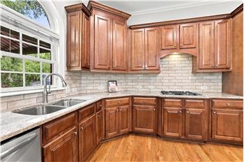 Kitchen features warm maple cabinets, 5-burner gas cooktop, hardwood floors, custom tile backsplash.