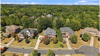 Aerial view of home and cul-de-sac street surrounded by impressive homes and mature trees stretching across the landscape.