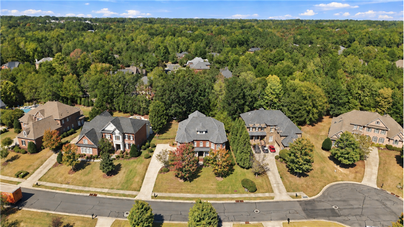 Aerial view of home and cul-de-sac street surrounded by impressive homes and mature trees stretching across the landscape.
