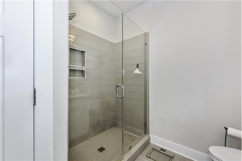 En-suite owner's bathroom features frameless, heavy glass pivot shower door, tile surround and tile floors.