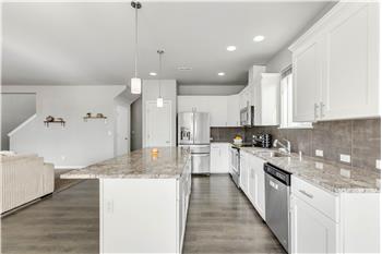 The kitchen island faces the cooking area, with a pantry, white cabinetry, and stainless-steel appliances all in view.