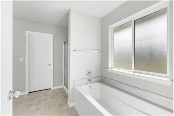 A separate bathtub and glass-enclosed shower round out the primary bath, with a frosted window above the tub.