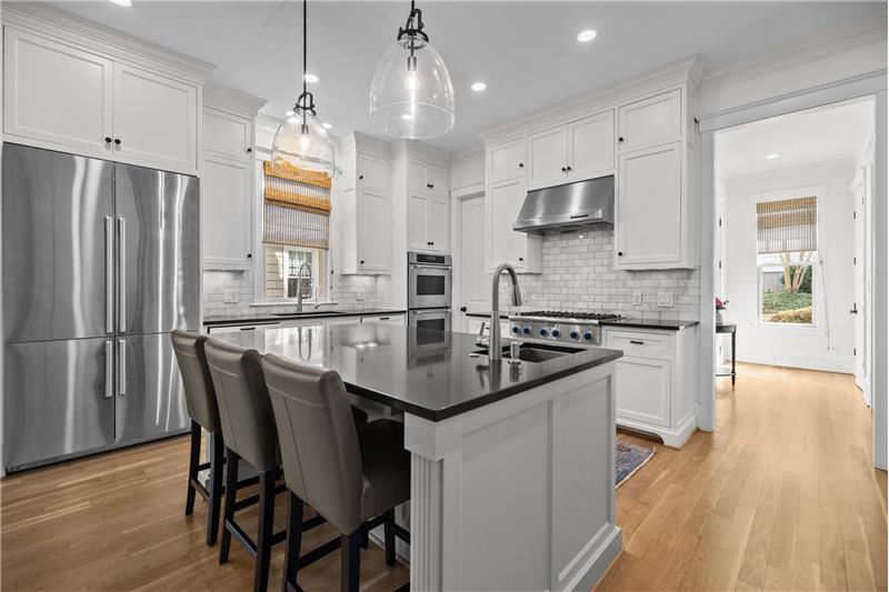Kitchen features island with seating, granite counters, tile backsplash, designer pendant lights, under-cabinet lights.