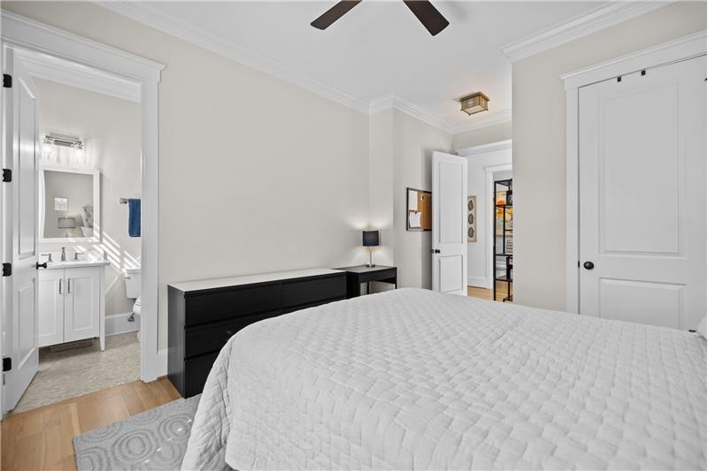 Main floor bedroom suite Features a private, en-suite bathroom, closet, hardwood floors, ceiling fan with light, crown molding.