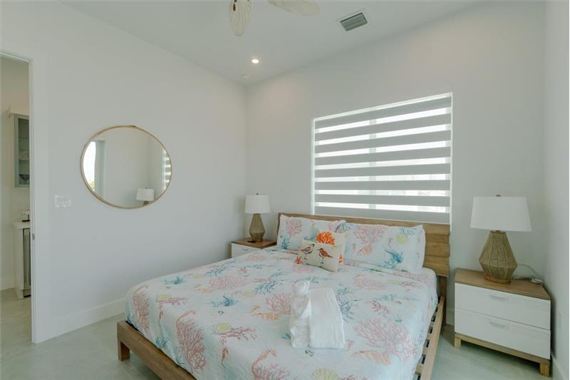 King bedroom with ensuite bathroom, smart TV, and access to balcony overlooking the pool and open water.