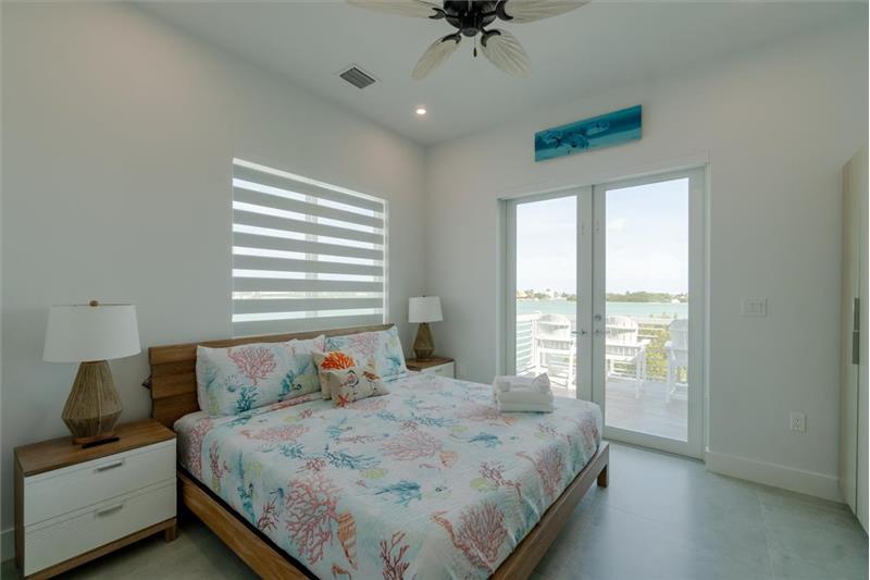 King bedroom with ensuite bathroom, smart TV, and access to balcony overlooking the pool and open water.