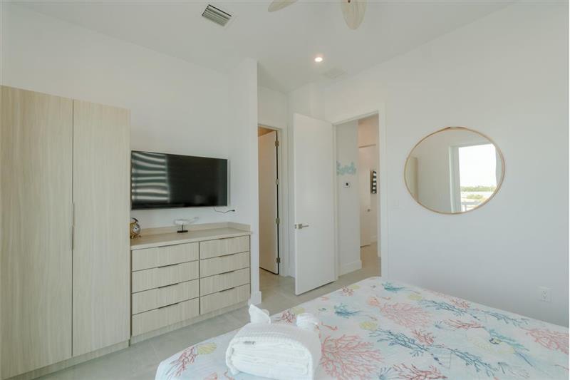 King bedroom with ensuite bathroom, smart TV, and access to balcony overlooking the pool and open water.