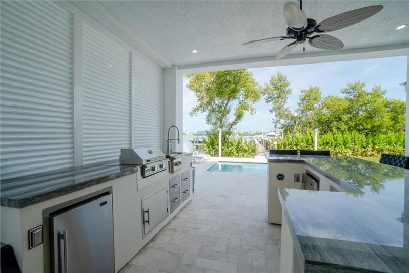 Outdoor kitchen with gas grill, wet bar, and mini refrigerators.