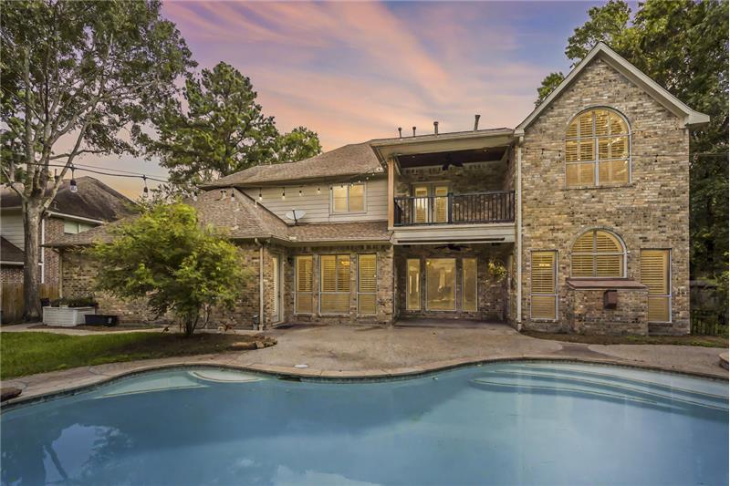 Charming home with a spacious backyard featuring a swimming pool. The house has large windows with shutters, a balcony, and a co