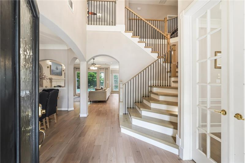 This inviting entryway features elegant hardwood flooring and a staircase with sleek railings. Arched doorways lead to a spaciou