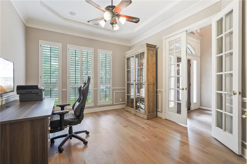 This room features hardwood floors, large windows with shutters for natural light, and French doors. It includes built-in shelvi