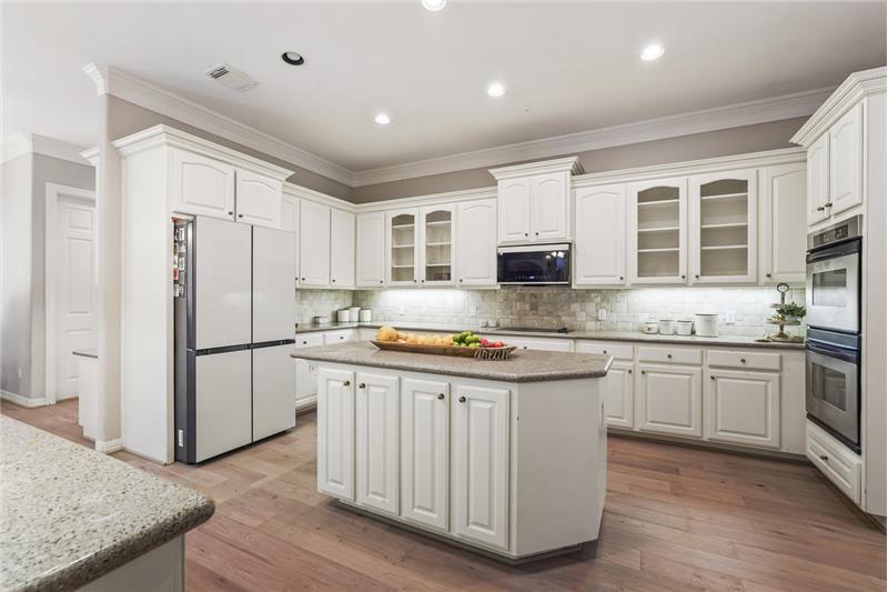 This spacious kitchen features elegant white cabinetry, a large central island, and top of the line appliances.