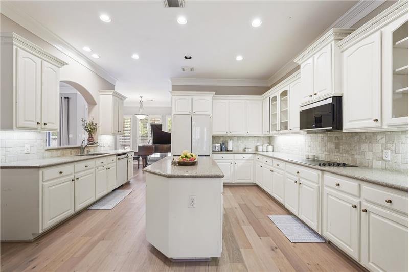 Spacious kitchen with white cabinetry, granite countertops, and hardwood floors. Features an island, built-in appliances, and re