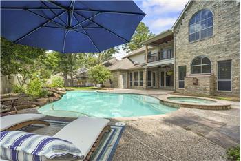 This inviting backyard features a spacious pool and hot tub, surrounded by a well-maintained patio area. The brick exterior of t