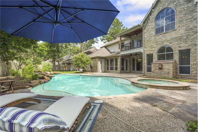 This inviting backyard features a spacious pool and hot tub, surrounded by a well-maintained patio area. The brick exterior of t