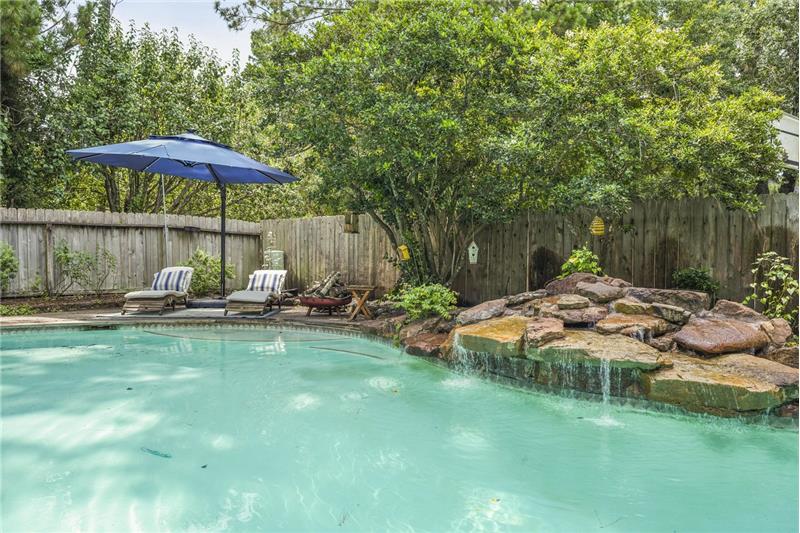 This backyard features a serene pool with a rock waterfall, surrounded by lush greenery offering a peaceful outdoor retreat.