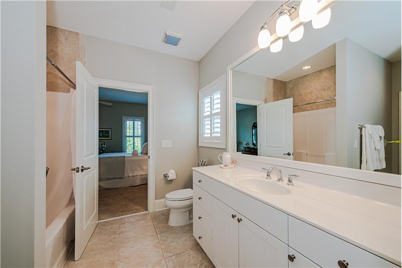 Jack & Jill bathroom features extended vanity with storage, tub-shower combination, tile floor, window with plantation shutters.