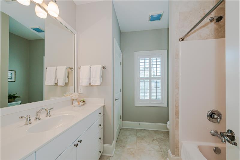 En-suite bathroom features extended vanity with storage, framed mirror, tub-shower, linen closet, tile flooring, window.
