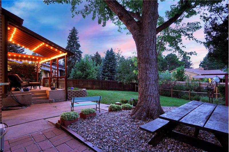 Sunset view of fenced backyard with a raised covered patio, an extended patio, and paver walk way