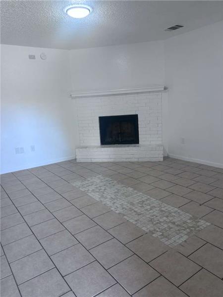 Unfurnished living room featuring a textured ceiling, light tile patterned floors, and a brick fireplace