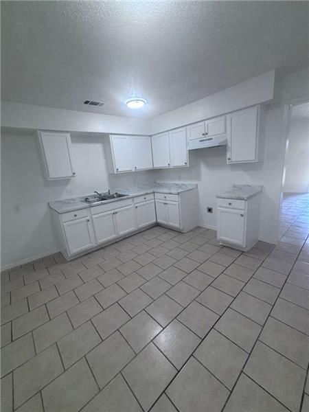 Kitchen featuring white cabinetry, light countertops, a textured ceiling, light tile patterned floors, and under cabinet range h