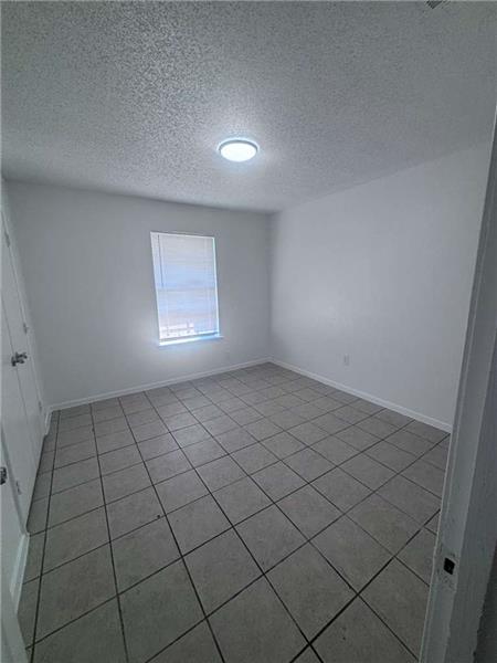 Empty room with a textured ceiling and light tile patterned floors