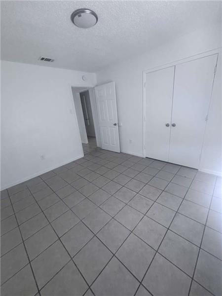 Unfurnished bedroom featuring a textured ceiling, light tile patterned floors, and a closet