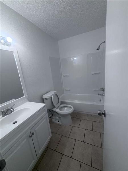 Bathroom with shower combination, light tile patterned floors, vanity, a textured ceiling, and a textured wall