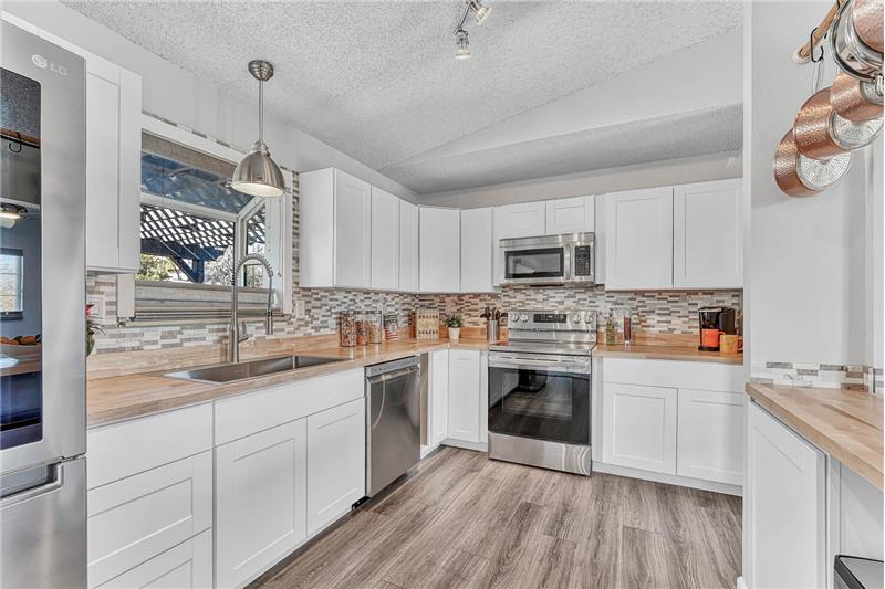 The Kitchen also features stainless steel appliances & white cabinets w/butcher block countertops & attractive stone backsplash