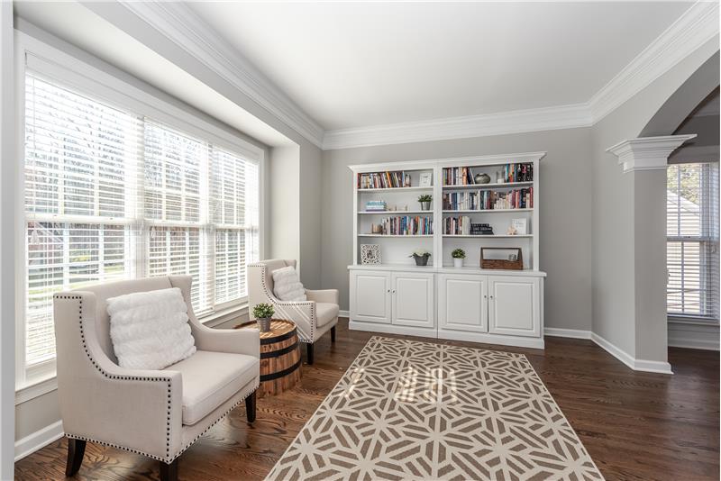 Bright and open living room with hardwood floors, crown molding, triple windows.