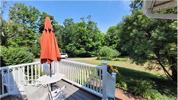 Porch with composite decking and white railings, offering views of a landscaped yard with mature trees