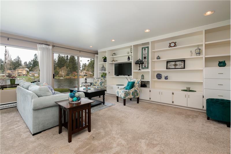 The open, airy living room features gorgeous lake views and custom cabinetry. Slider out to patio, lawn, dock and lake!!
