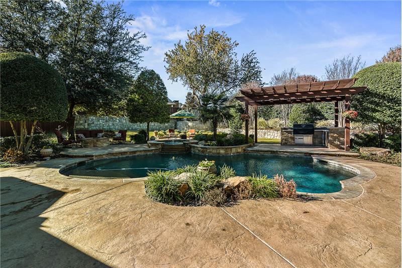 Your backyard oasis awaits with pool, spa, multiple patios, green grass, and outdoor kitchen.