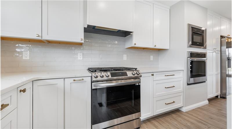 burner gas range/oven with range hood vented to the outside. Microwave/convection oven and wall oven to the right.