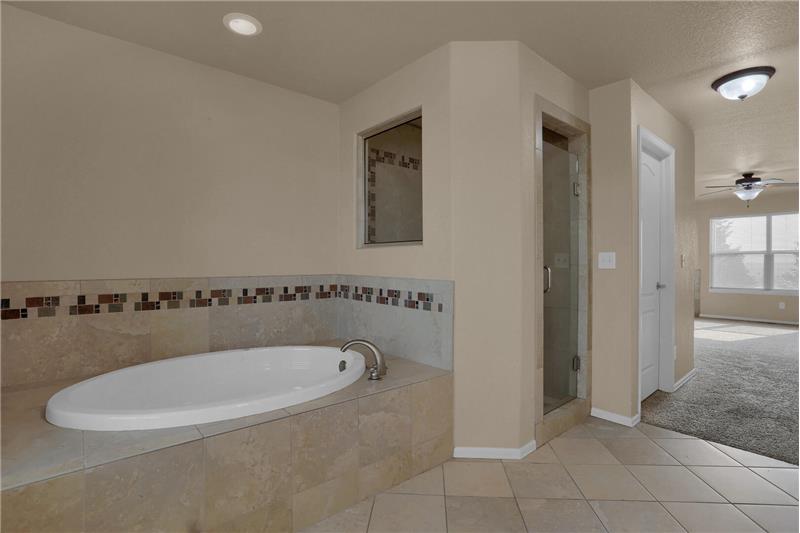 Master bath features tile flooring, fully tiled shower (including pan) with a bench and window, and a soaking tub