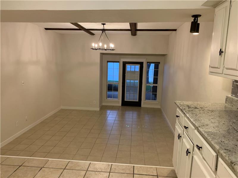 Downstairs Unfurnished Living area & dining area with light tile patterned floors, beam ceiling, a chandelier, and coffered ceil