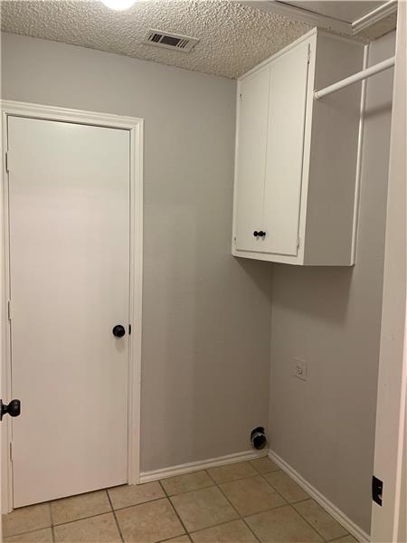 Laundry room with cabinet space, light tile patterned floors, hookup for an electric dryer, and a textured ceiling