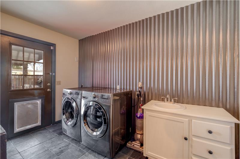 Laundry room with sink, slate tile flooring, and dog door access to fenced backyard