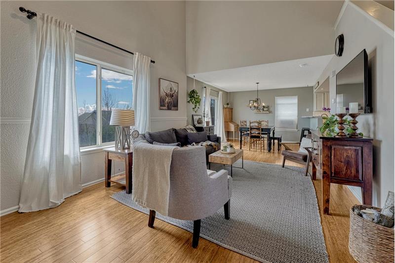 The Living Room boasts tall ceilings, beautiful bamboo flooring, and a large window with backyard views.