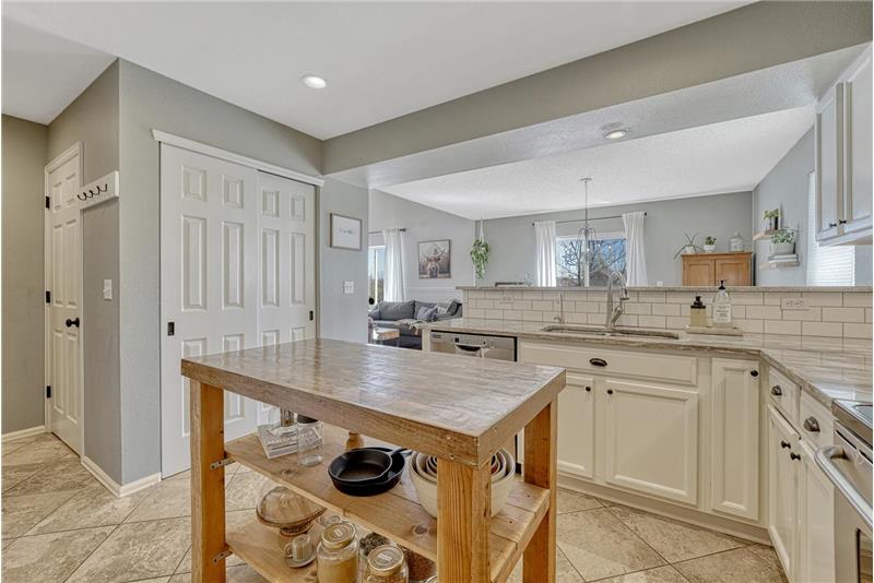 Kitchen with tile floors, a pantry, & white cabinets with granite countertops.