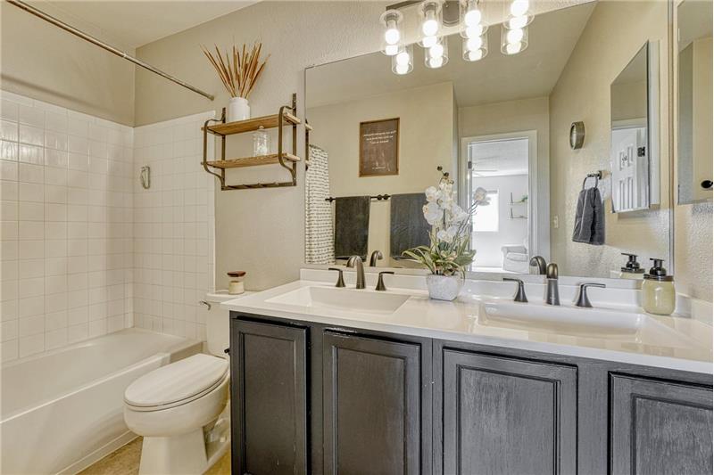 Primary Bathroom with updated dual sink vanity, mirror, and tiled tub/shower.
