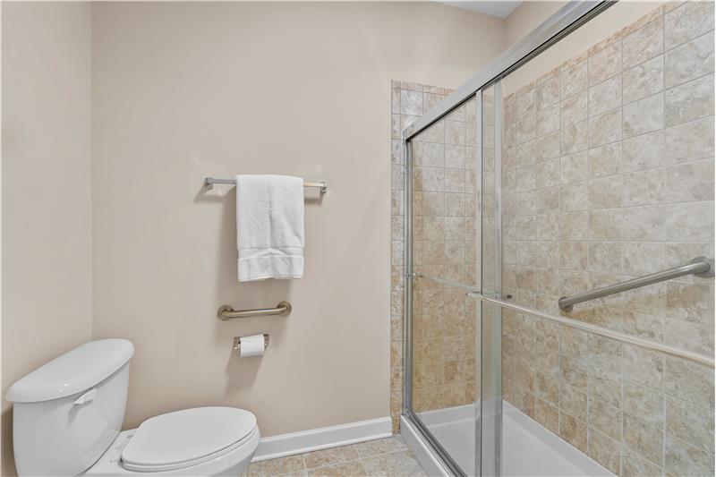 Primary bathroom with tile flooring, tile shower surround, grab bars for safety