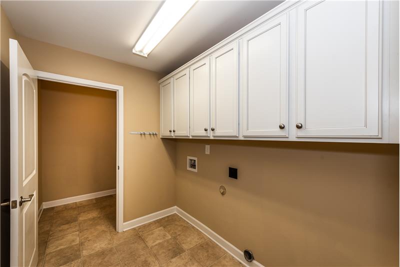 Large laundry room with full wall of cabinets; large storage room behind the laundry.