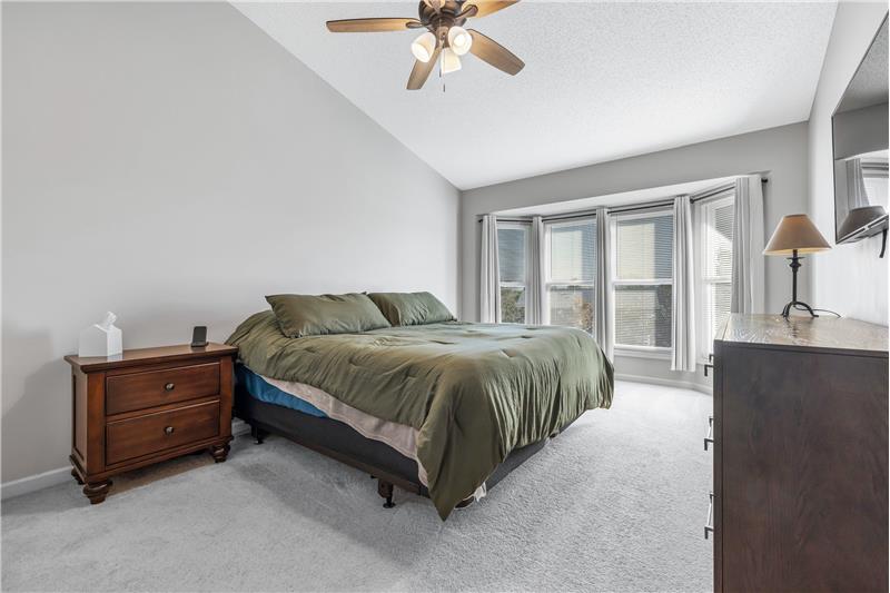 Primary bedroom with ceiling fan and bay window