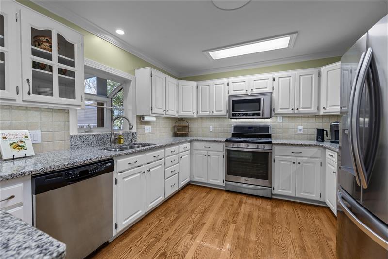 Well-appointed, functional 
kitchen has white cabinets, granite counters, stainless appliances, garden window, hardwood floors.