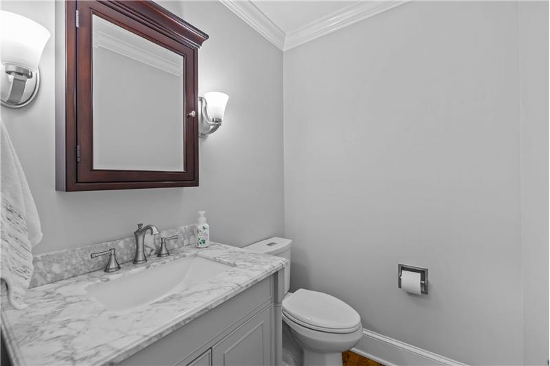 Remodeled powder room includes new vanity, toilet, light fixtures, mirror. Neutral paint, hardwood floor, crown molding.